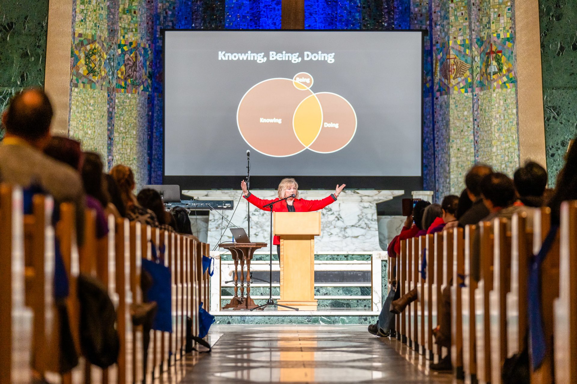 A woman at a pulpit teaches a large congregation.