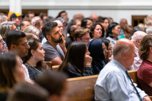 A large crowd is gathered. A man places his head in his hands, deep in thought.