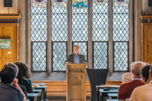 A man at a pulpit with a tall window behind him