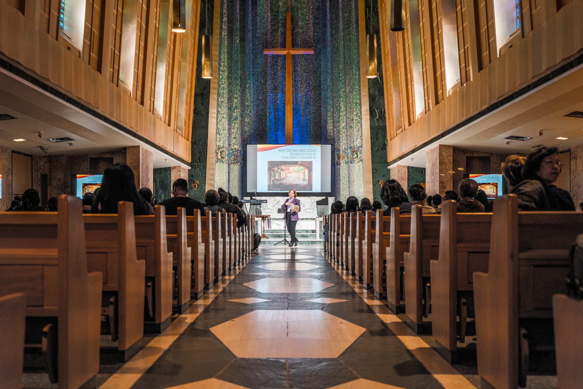 A woman with the spotlight on her teaches in a dimly lit chapel
