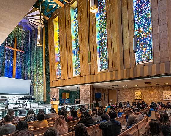 Crowded church with light pouring through stained glass windows